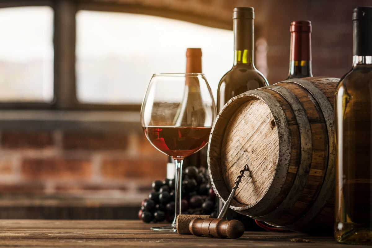 Glas Rotwein neben Mehrwegflaschen und Holzfass